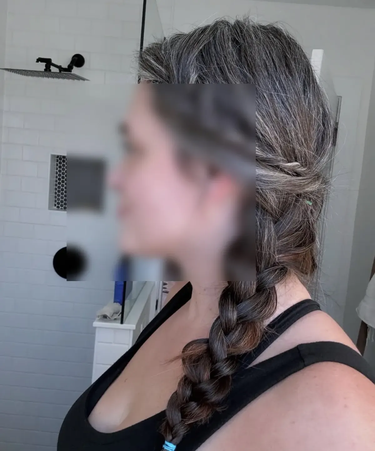 Side portrait of a person with braided hair and blurred face in a bathroom, suggesting discretion for kink dating profiles